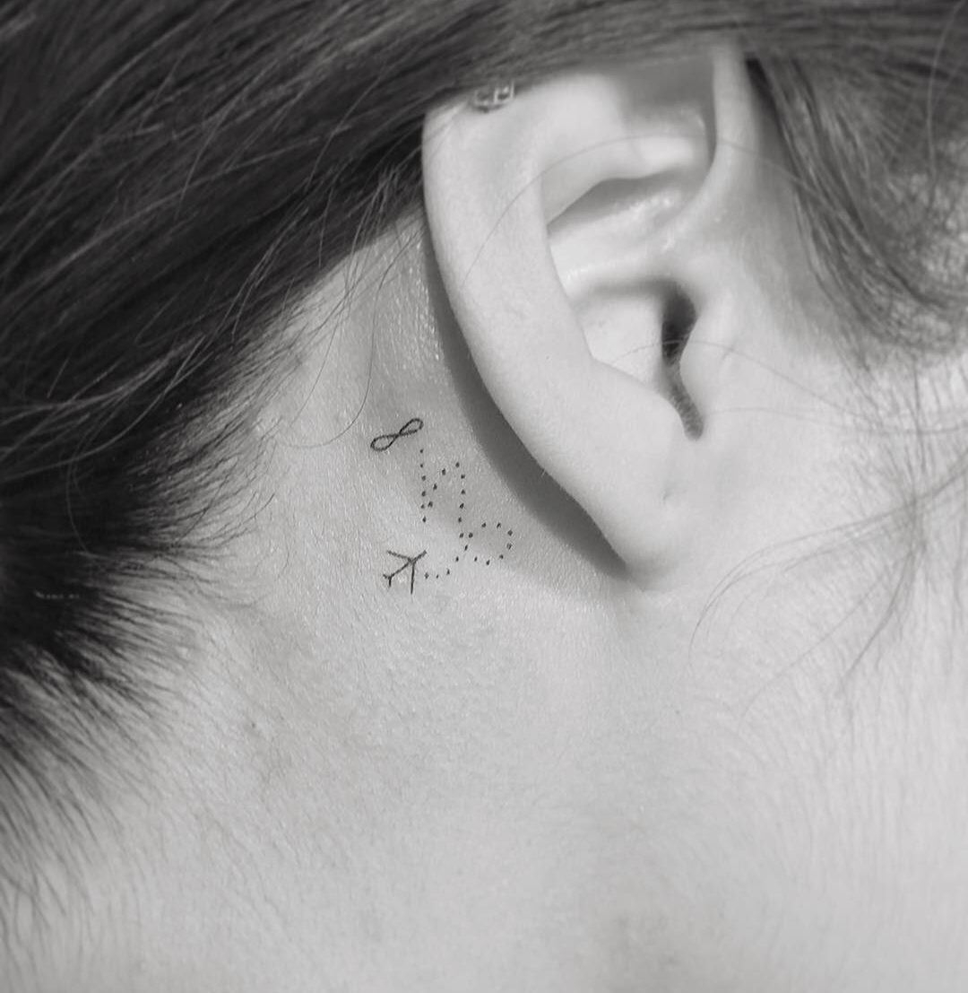 Tiny infinity and Capricorn zodiac symbol tattoo behind the ear