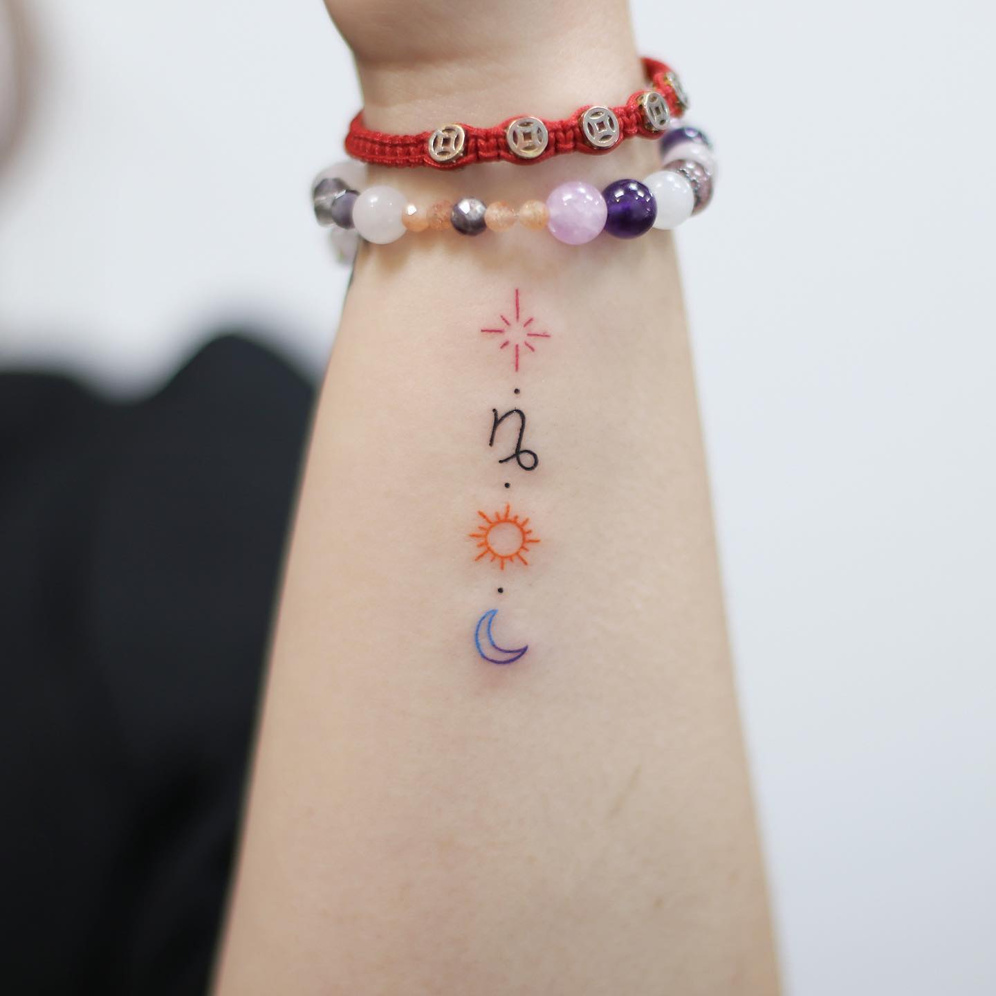 Minimalist style Capricorn symbol, star, sun, and moon tattoo on the wrist