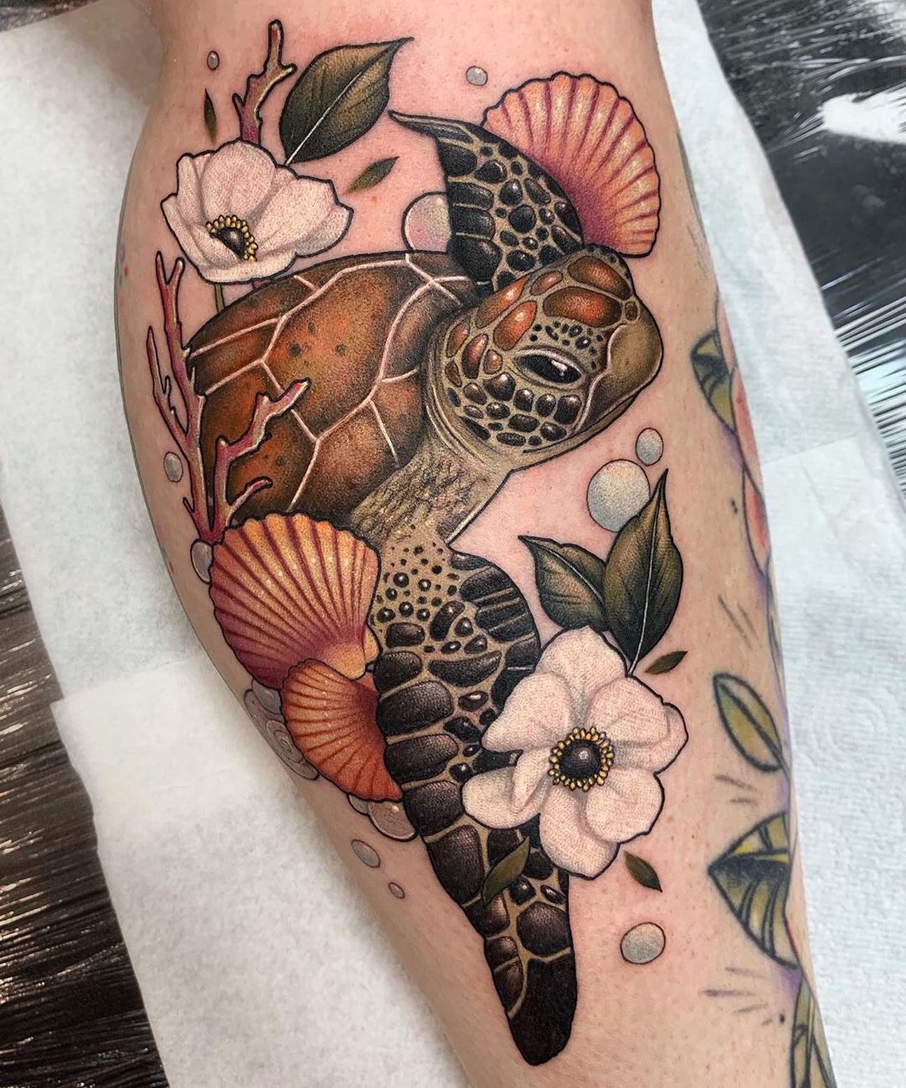 Watercolor style sea turtle tattoo with shells and flowers on the calf