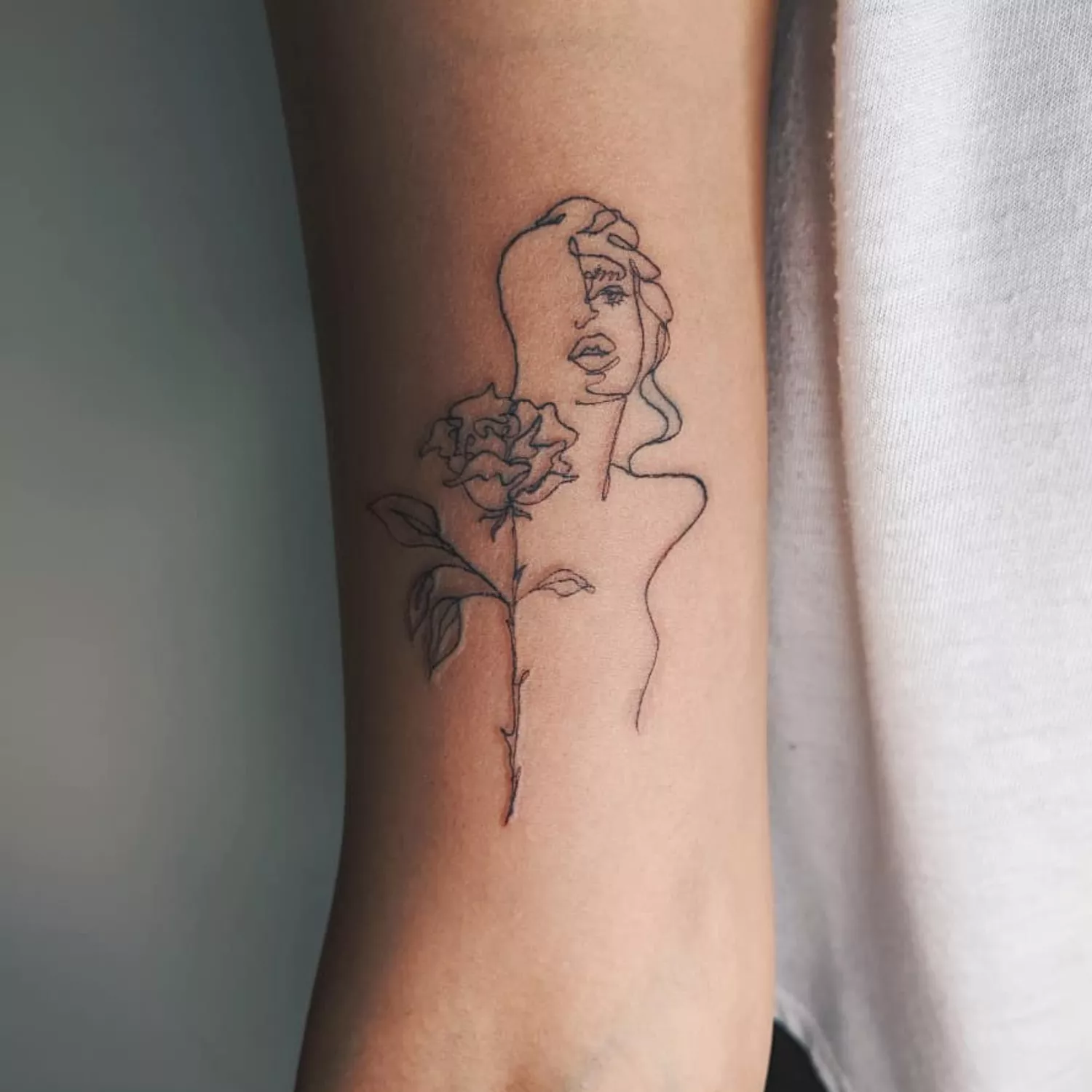 A close up of a portrait tattoo of a woman paired with a rose.