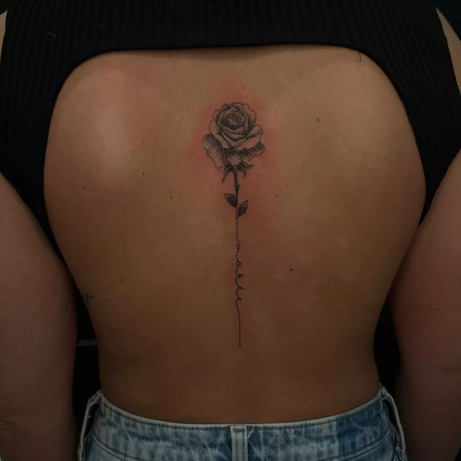 A close up of a rose stem tattoo on the spine.