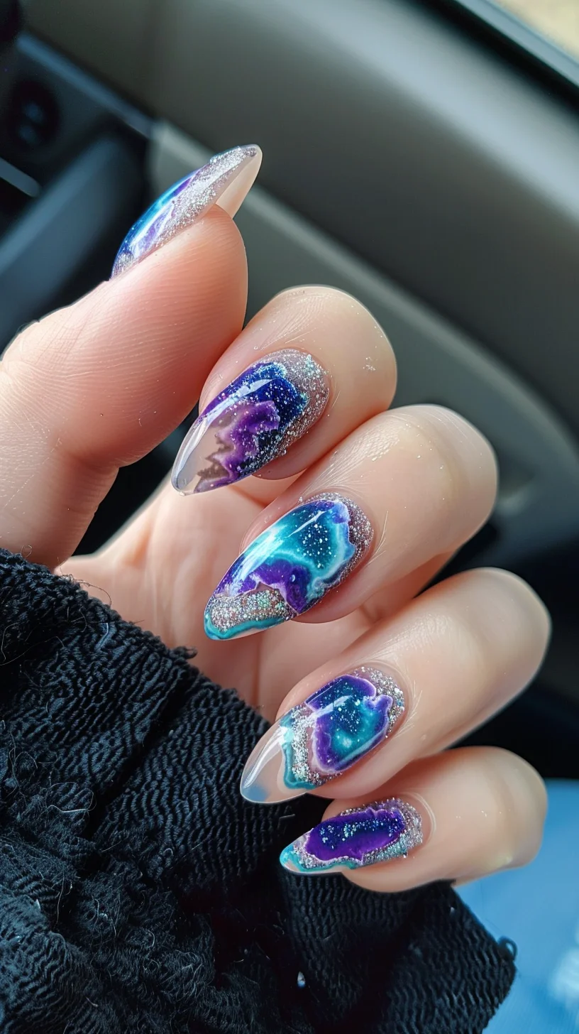 This geode nail art design captivates with its stunning blend of deep blues and purples, complemented by crystalline and silvery accents. The nails feature a glossy finish with translucent tips, transitioning into vivid, saturated colors that mimic the natural layering of geode stones. Silver glitter traces the outlines of each geode section, adding a sparkling contrast that enhances the depth and realism of the design.