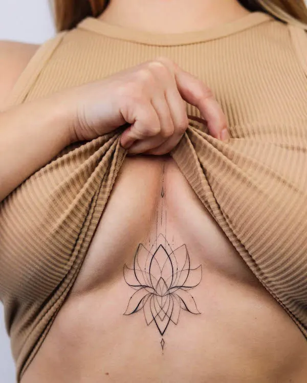 Lotus outline between breast tattoo by @dasha_sumtattoo