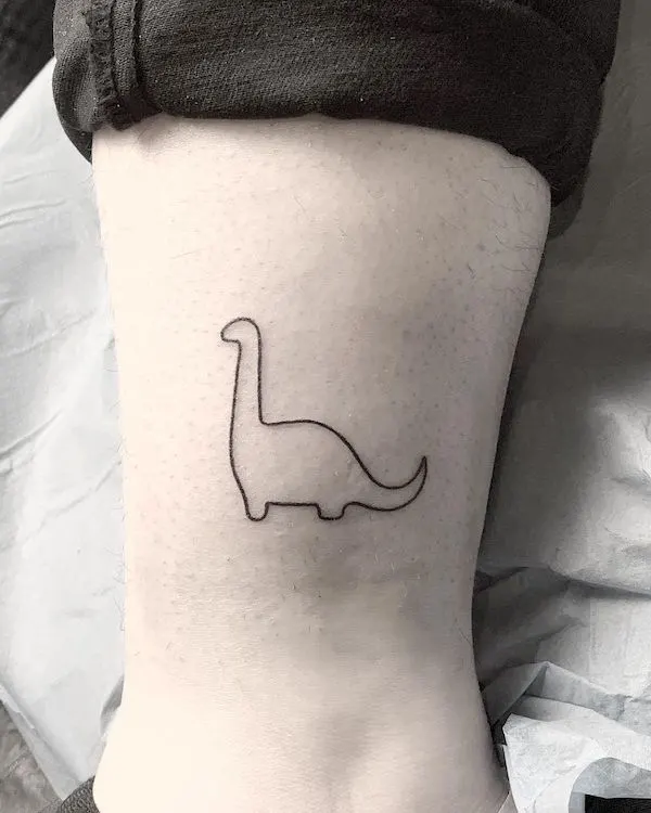 Minimalist small dinosaur tattoo above the ankle by @alekstattooer