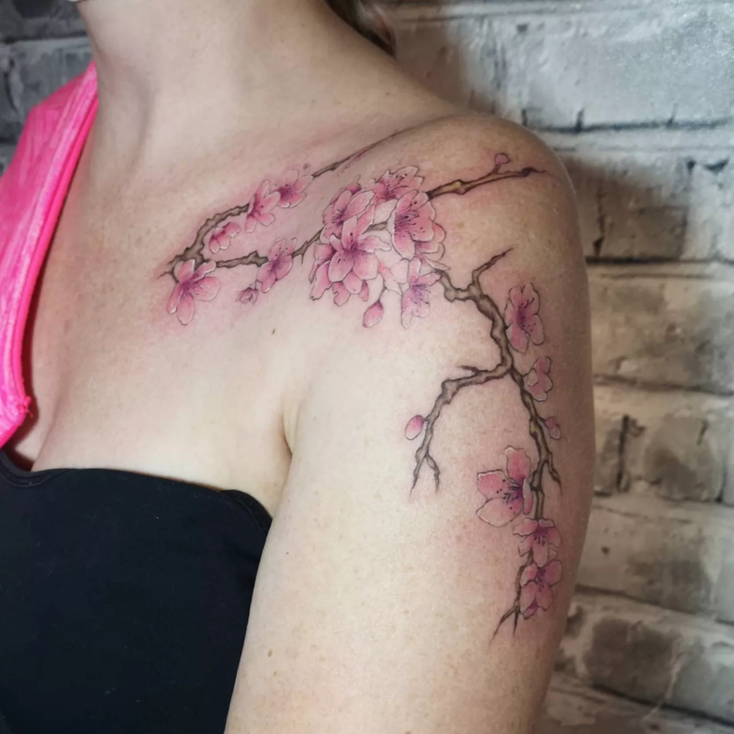 zoomed-in image of model with large cherry blossom tattoo starting on collarbone and cascading down shoulder and arm, in shades of pink and brown