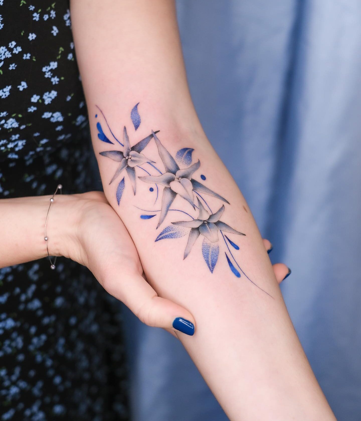 Blue orchids tattooed on the inner forearm, illustrative style