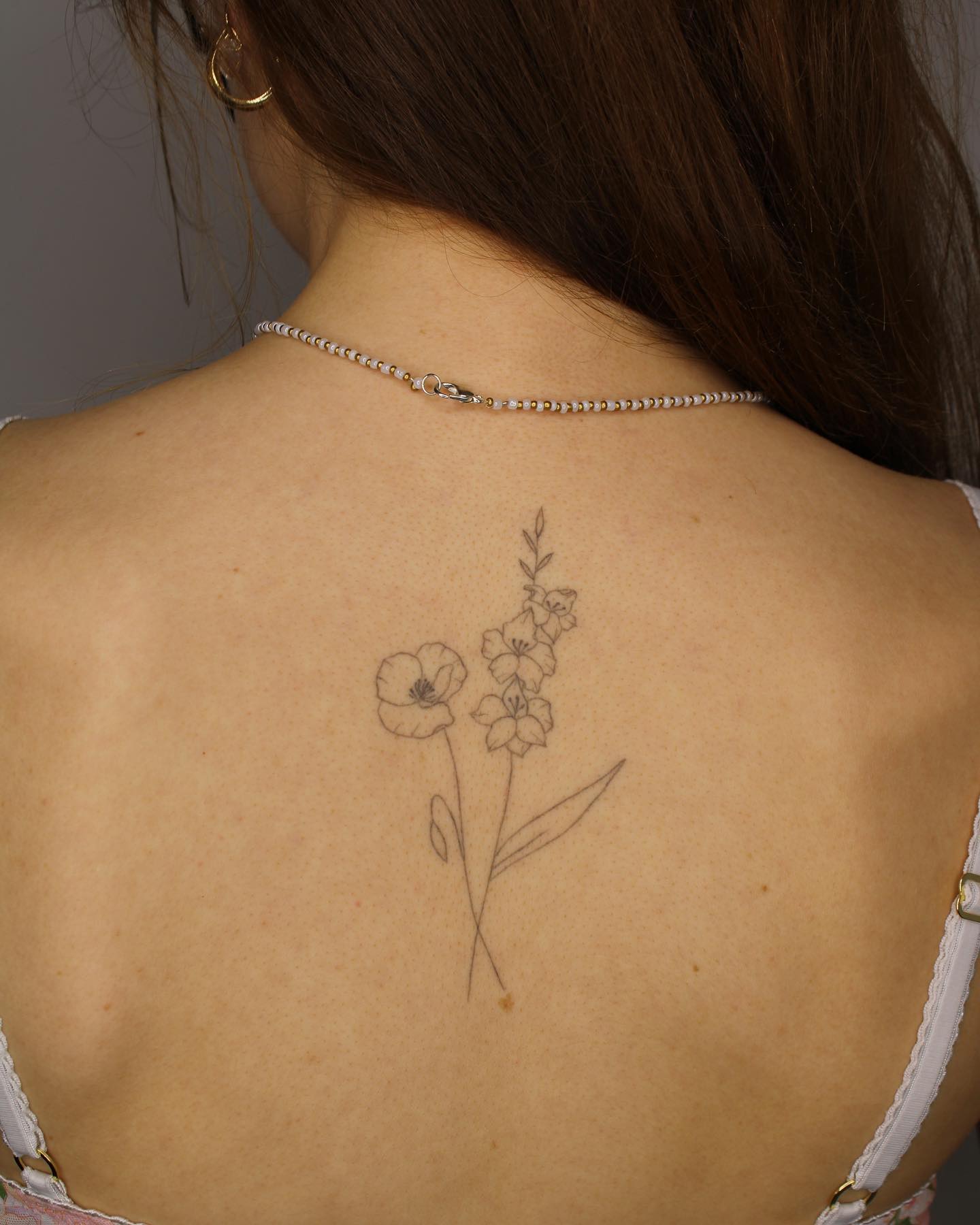 Fine line style poppy and lilies tattooed on the upper back