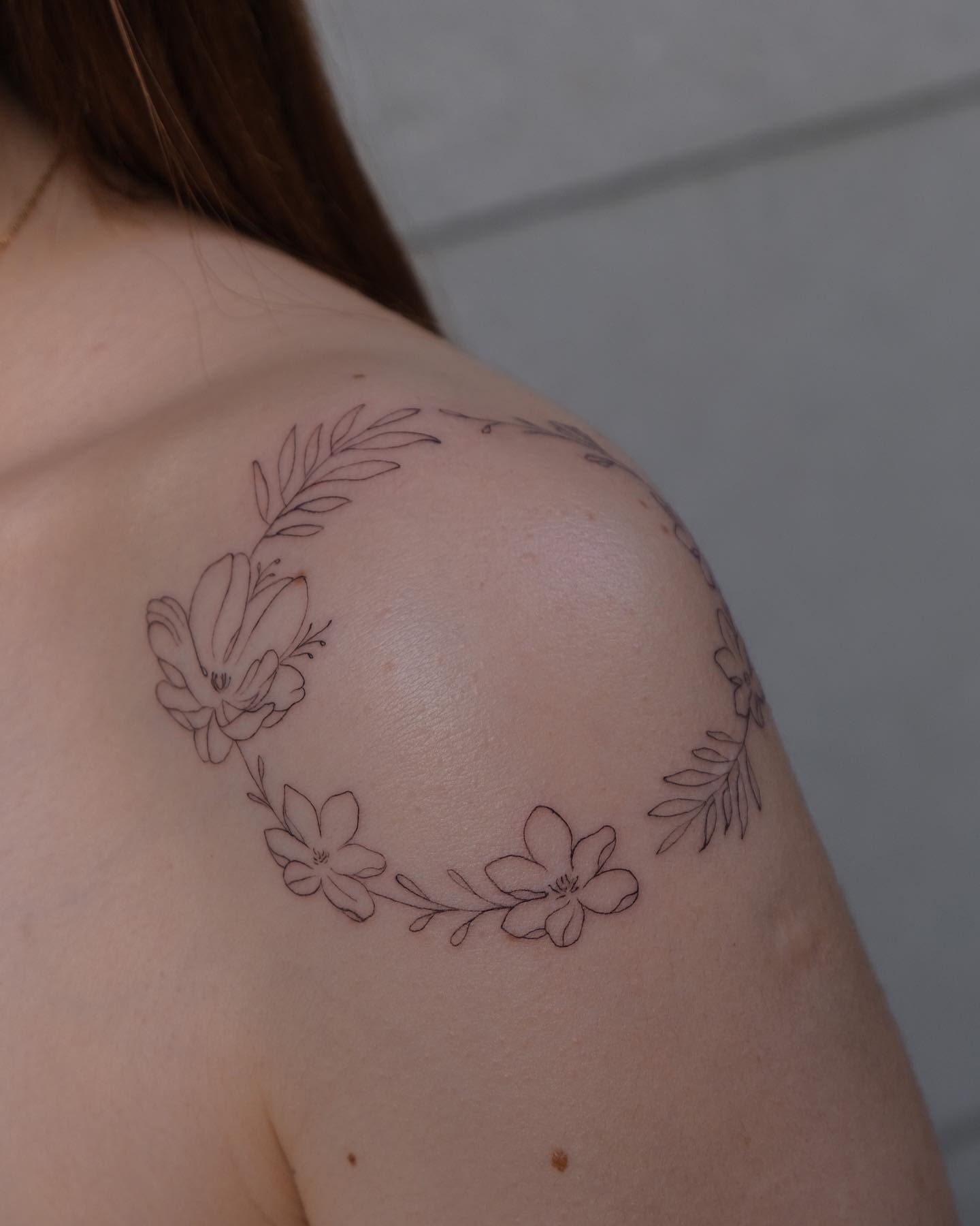 Fine line style flower wreath tattoo on the shoulder