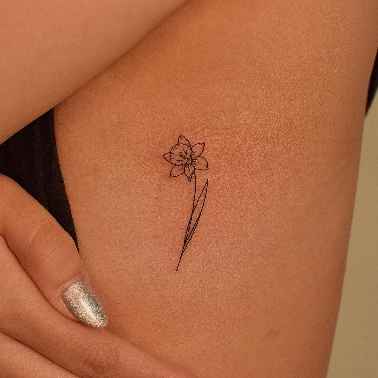 Daffodil tattoo located on the sideboob, fine line style